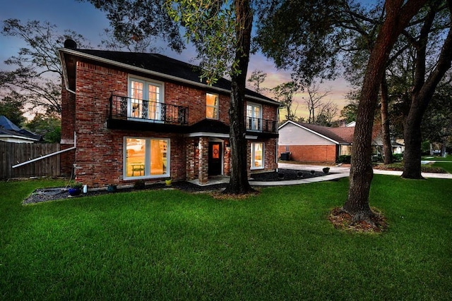 back house at dusk with a lawn and a balcony