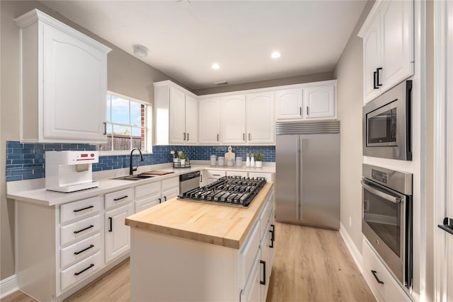 kitchen featuring wood counters, white cabinetry, a center island, built in appliances, and sink