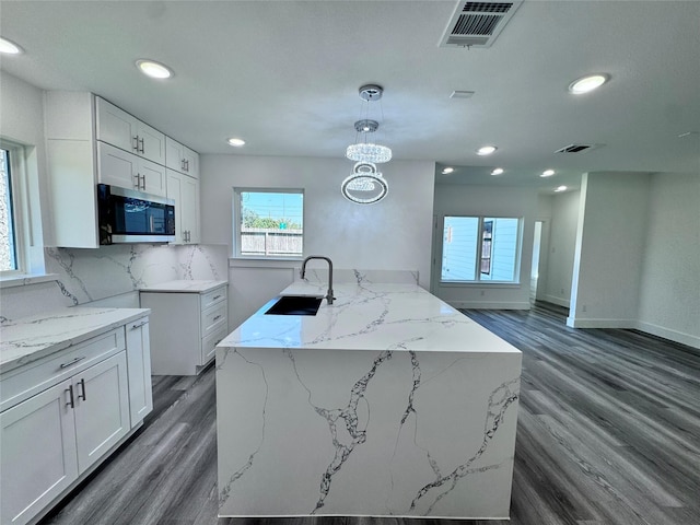 kitchen with white cabinets, decorative light fixtures, a center island with sink, and sink