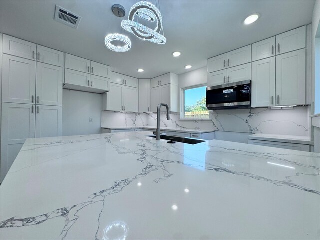 kitchen featuring light stone countertops, sink, pendant lighting, decorative backsplash, and white cabinets