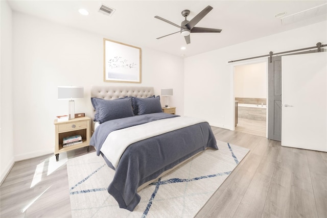 bedroom featuring ceiling fan, light wood-type flooring, ensuite bathroom, and a barn door