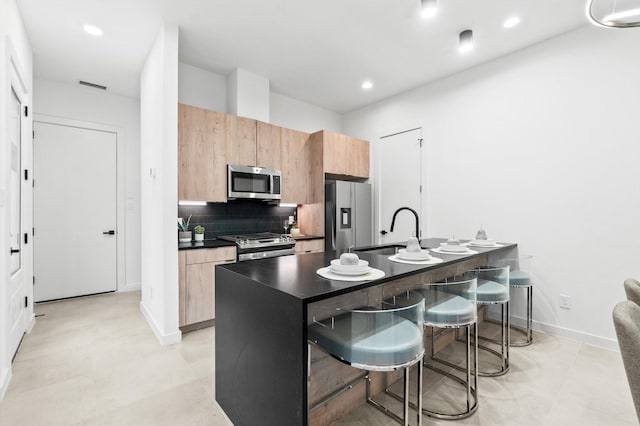 kitchen featuring sink, tasteful backsplash, a breakfast bar area, a center island with sink, and appliances with stainless steel finishes