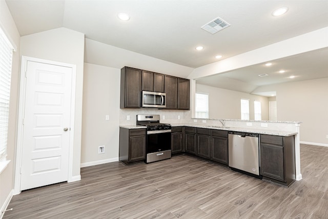 kitchen with kitchen peninsula, sink, stainless steel appliances, and vaulted ceiling