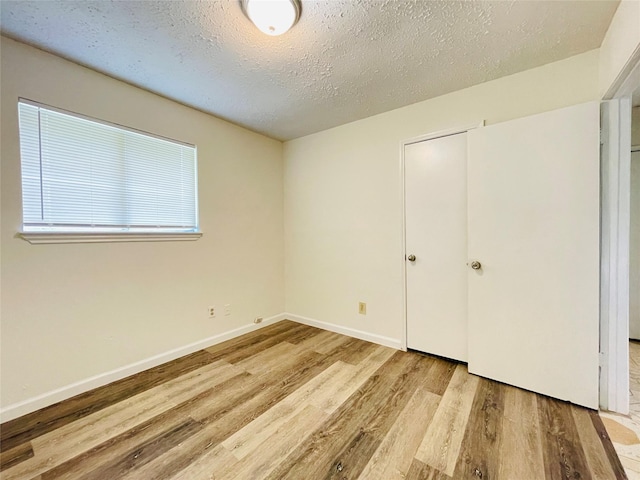 unfurnished bedroom featuring light hardwood / wood-style floors, a textured ceiling, and a closet