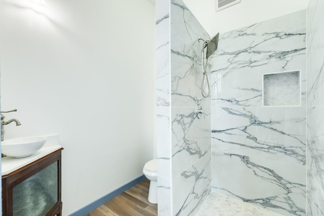 bathroom with a tile shower, vanity, toilet, and wood-type flooring