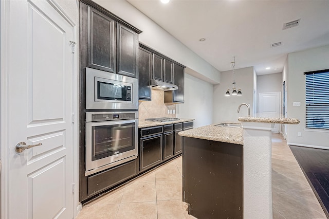 kitchen with decorative backsplash, appliances with stainless steel finishes, a kitchen island with sink, sink, and light tile patterned floors