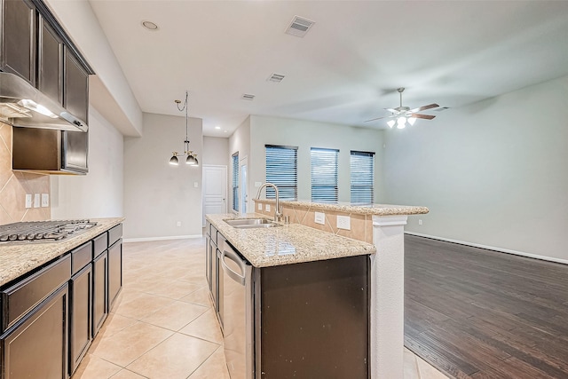 kitchen with appliances with stainless steel finishes, light stone counters, ceiling fan, sink, and an island with sink