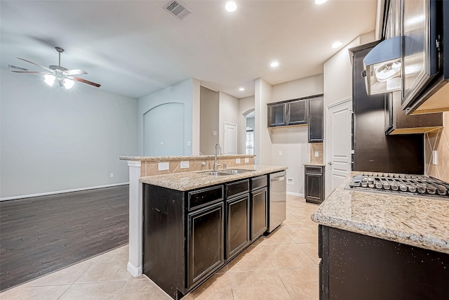 kitchen with light stone countertops, sink, stainless steel appliances, a center island with sink, and light tile patterned flooring