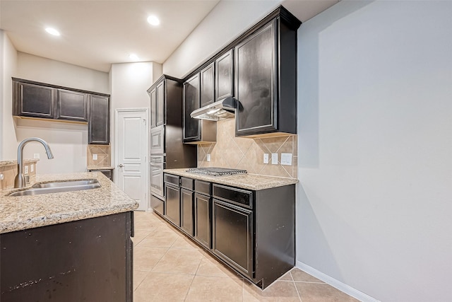 kitchen with sink, stainless steel appliances, light stone counters, backsplash, and light tile patterned floors