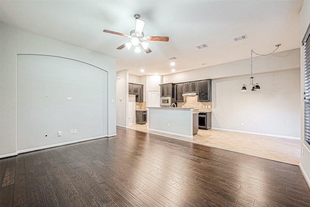 unfurnished living room featuring ceiling fan with notable chandelier and hardwood / wood-style flooring