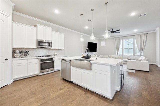 kitchen with crown molding, an island with sink, pendant lighting, stainless steel appliances, and white cabinets