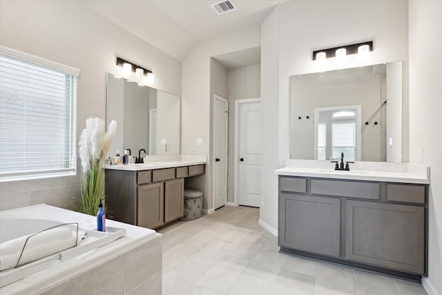 bathroom with vanity, tile patterned floors, lofted ceiling, and tiled bath