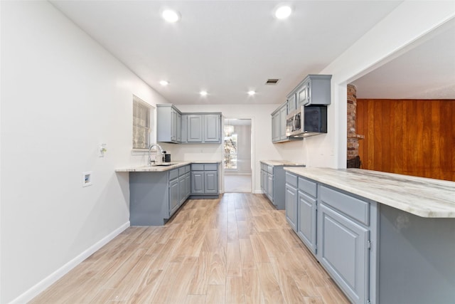 kitchen with gray cabinetry, light stone countertops, sink, kitchen peninsula, and light hardwood / wood-style floors