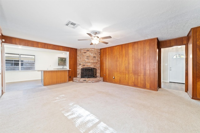 unfurnished living room featuring a fireplace, light carpet, ceiling fan, and wood walls