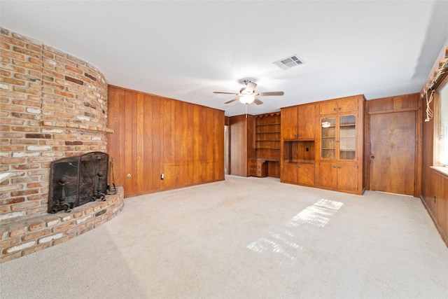 unfurnished living room featuring ceiling fan, wood walls, light colored carpet, and a fireplace