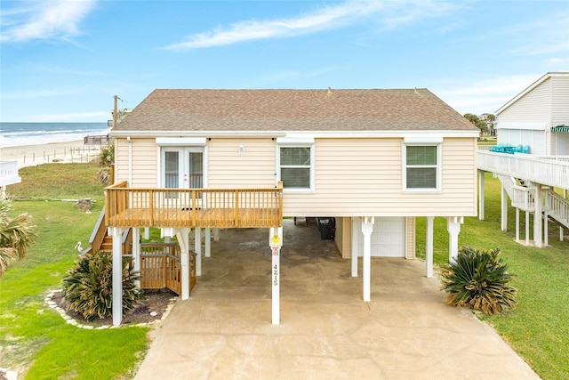 view of front of property featuring french doors, a front lawn, a view of the beach, a water view, and a garage