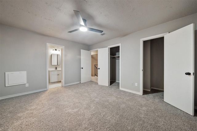 unfurnished bedroom with ensuite bathroom, a textured ceiling, ceiling fan, and carpet