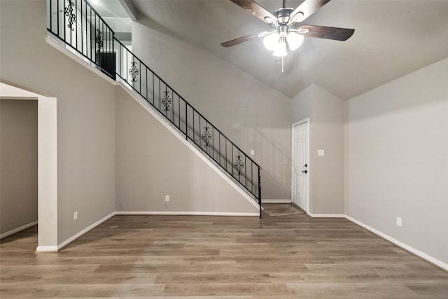 unfurnished living room featuring ceiling fan, light wood-type flooring, and a towering ceiling