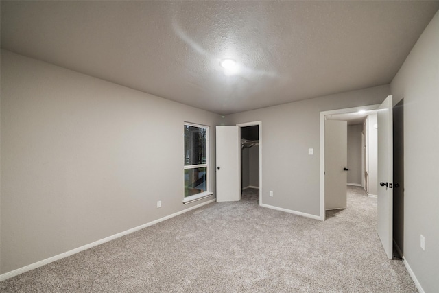 unfurnished bedroom featuring a textured ceiling, a spacious closet, a closet, and light carpet