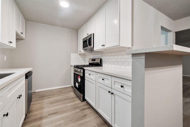 kitchen featuring stainless steel appliances, light stone countertops, light hardwood / wood-style flooring, white cabinetry, and tasteful backsplash