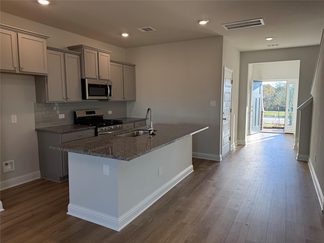 kitchen featuring a kitchen island with sink, sink, dark stone counters, and appliances with stainless steel finishes