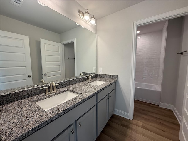 bathroom with hardwood / wood-style flooring, vanity, and tiled shower / bath