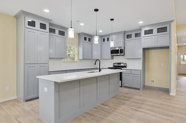 kitchen with hanging light fixtures, sink, stainless steel appliances, and a center island with sink