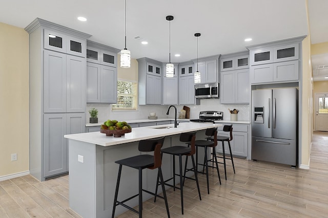 kitchen featuring sink, an island with sink, pendant lighting, a kitchen bar, and appliances with stainless steel finishes