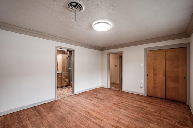 unfurnished bedroom featuring a textured ceiling, crown molding, hardwood / wood-style flooring, connected bathroom, and a closet