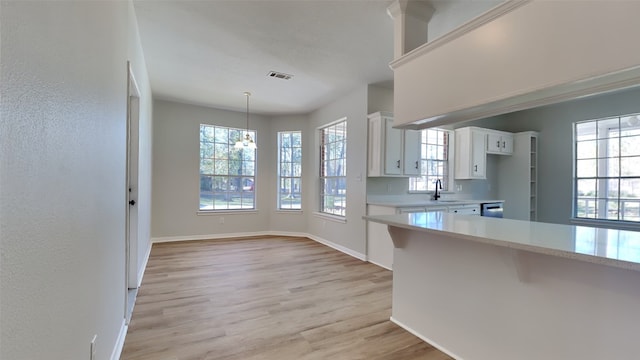 kitchen with sink, decorative light fixtures, light hardwood / wood-style floors, white cabinetry, and a breakfast bar area