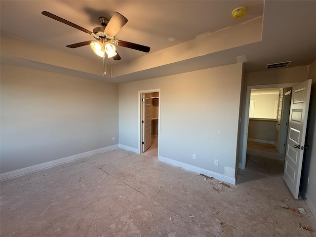 unfurnished bedroom featuring a closet, a walk in closet, a tray ceiling, and ceiling fan