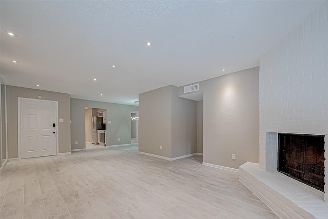 unfurnished living room with a brick fireplace, a textured ceiling, and light hardwood / wood-style flooring