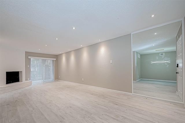 unfurnished living room featuring a fireplace, a textured ceiling, and light hardwood / wood-style floors