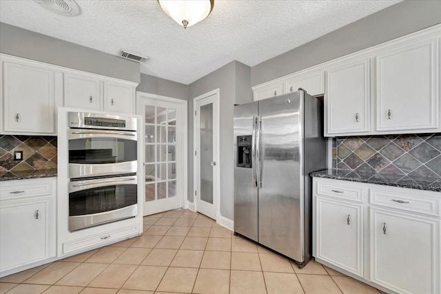 kitchen featuring white cabinets, stainless steel appliances, dark stone counters, and tasteful backsplash