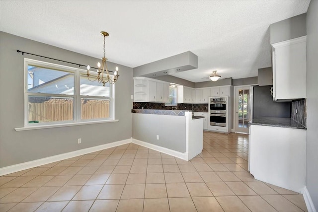 kitchen featuring decorative backsplash, light tile patterned flooring, white cabinetry, and an inviting chandelier