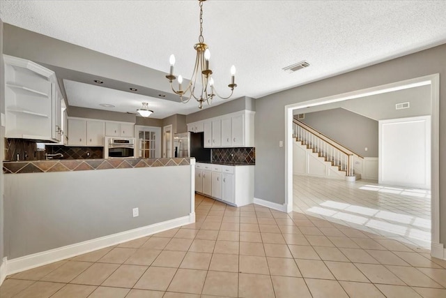 kitchen with white cabinetry, stainless steel appliances, a chandelier, decorative backsplash, and light tile patterned flooring