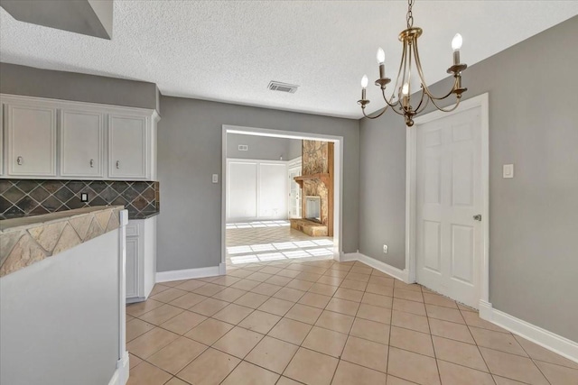 unfurnished dining area with light tile patterned floors, a textured ceiling, and a notable chandelier