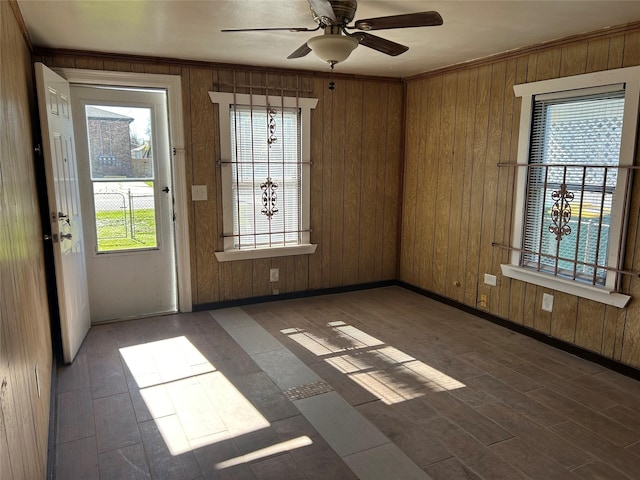 unfurnished room with wooden walls, ceiling fan, a healthy amount of sunlight, and ornamental molding