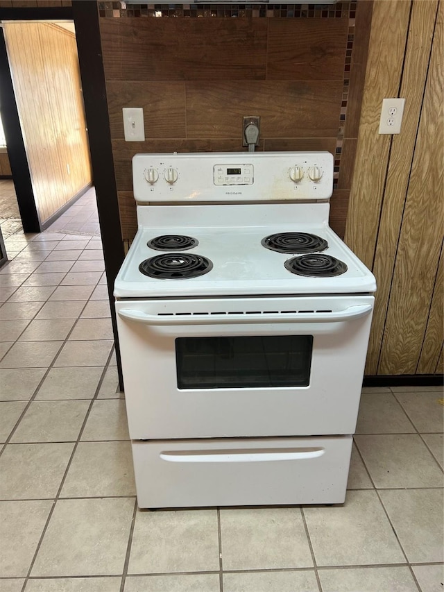 kitchen featuring wood walls, light tile patterned flooring, and white electric stove