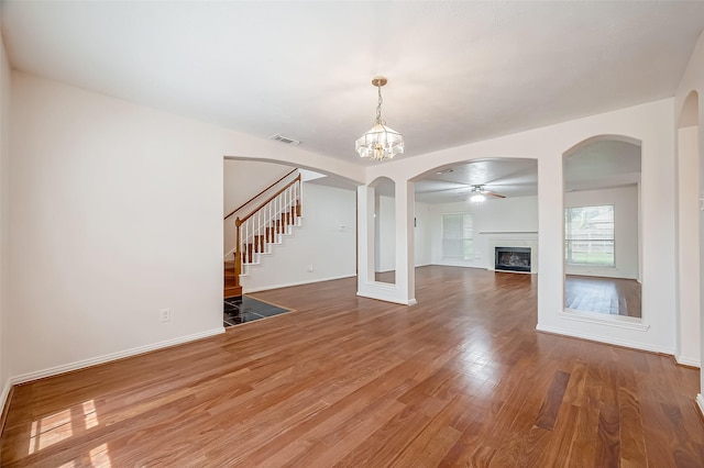 unfurnished living room featuring wood-type flooring and ceiling fan with notable chandelier