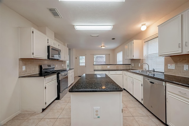 kitchen with stainless steel appliances, sink, white cabinets, a center island, and light tile patterned flooring