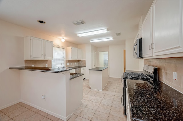 kitchen featuring white cabinets, stainless steel gas range, light tile patterned floors, tasteful backsplash, and kitchen peninsula