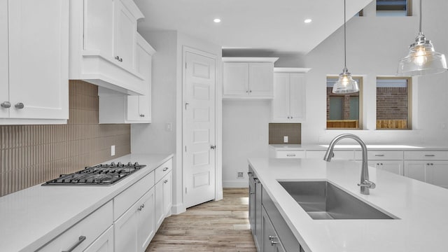 kitchen featuring light countertops, a sink, hanging light fixtures, and white cabinetry