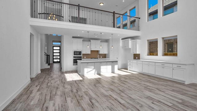 kitchen with appliances with stainless steel finishes, light wood-type flooring, white cabinets, and a kitchen island with sink