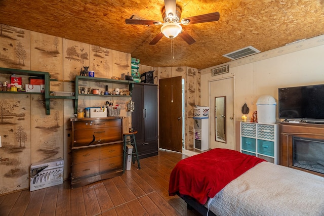 bedroom with ceiling fan, dark hardwood / wood-style flooring, wooden ceiling, and wood walls