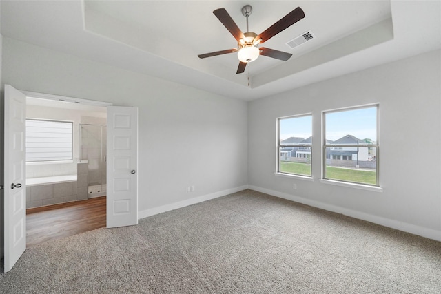 unfurnished bedroom with ceiling fan, carpet floors, and a tray ceiling