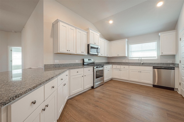 kitchen with light stone countertops, white cabinets, lofted ceiling, and appliances with stainless steel finishes