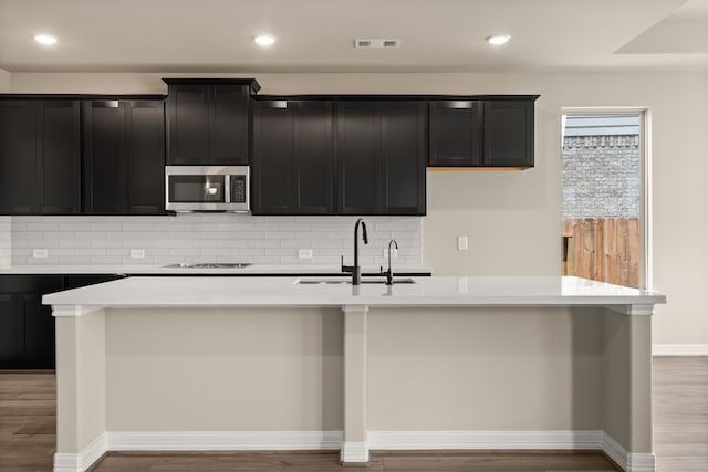 kitchen with hardwood / wood-style floors, sink, backsplash, and an island with sink