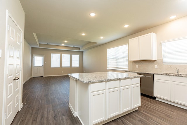 kitchen with stainless steel dishwasher, a raised ceiling, dark wood-type flooring, white cabinetry, and a kitchen island