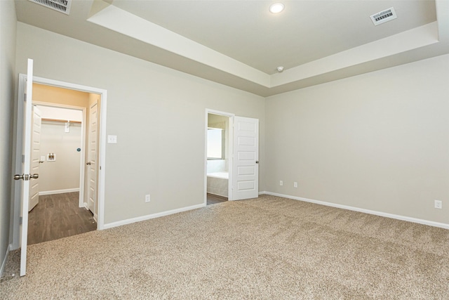 unfurnished bedroom with a walk in closet, ensuite bath, carpet floors, and a tray ceiling